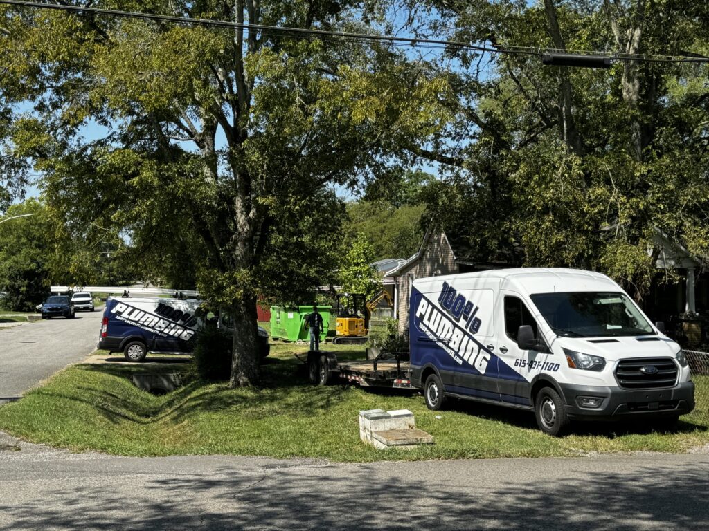 Two 100 Percent Plumbing vans, a trailer and a mini excavator on a residential job site in Nashville